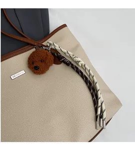 Close-up of beige canvas tote with brown leather edges and teddy bear charm