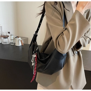 Detail of black PU leather half-moon shoulder bag with silver key charm and tassel decoration