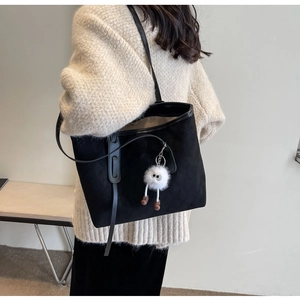 Close-up of black velvet tote bag featuring a cute white plush monster charm accessory