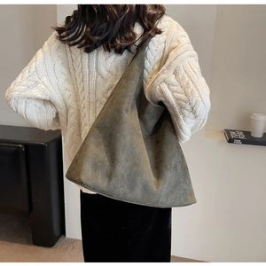 Detailed texture of a dark olive green suede tote bag worn by a model in a minimal room