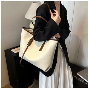 Detail of a large cream PU tote bag with brown contrast straps shown on a model