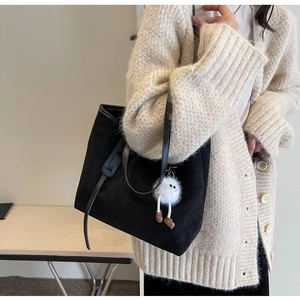 Detail of minimalist black velvet tote bag featuring a cute white plush monster charm