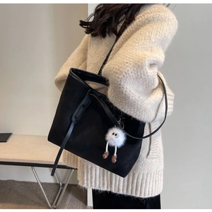 Detailed view of black velvet tote bag with cute white plush monster charm on model