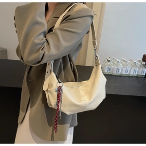 Detail of a creamy white half-moon hobo bag featuring soft pleats and metal chain charm