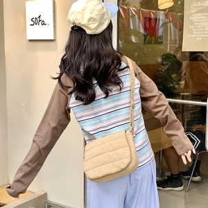 Detailed texture of beige quilted fabric crossbody bag with adjustable shoulder strap