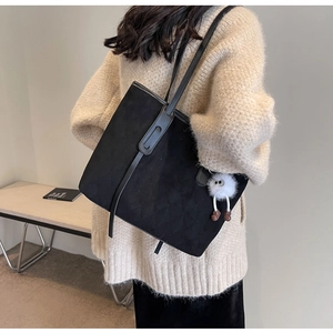 Detail view of black quilted faux suede tote bag with cute fluffy charm on model