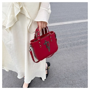 Detailed view of red PU handbag with silver rivets, metal cross charm and chain accents