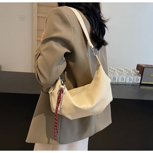 Close-up of minimalist cream PU leather crossbody bag with a red woven rope charm detail