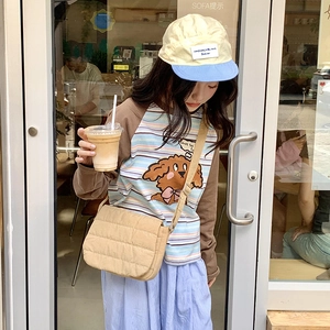 Detailed view of a beige quilted crossbody bag styled with casual striped long sleeve outfit