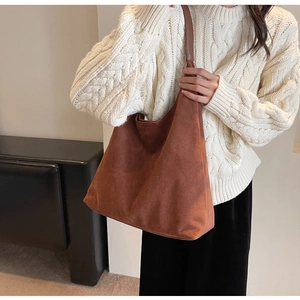 Detailed view of caramel suede tote bag worn on shoulder with cream knit sweater