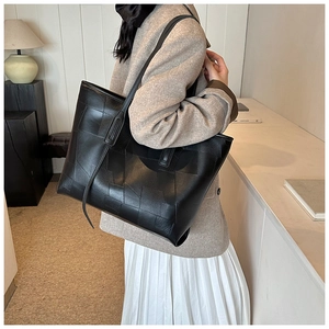 Detail of a black textured tote bag with square pattern worn by a model in a minimalist setting