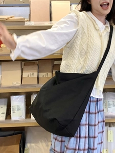 Close-up of a large black canvas crossbody bag with a wide strap shown on a model