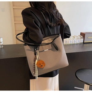 Detail of grey PU leather tote bag with black shoulder straps and plush bear charm