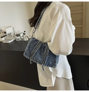 Detailed view of casual blue denim crossbody bag with multiple utility zippers on a model