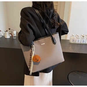 Detail view of grey canvas tote bag with black faux leather trim and plush bear charm