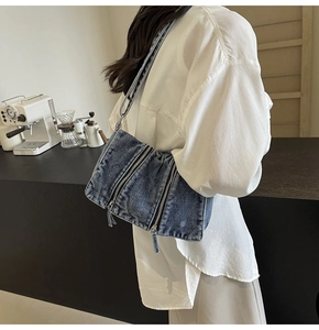 Detail view of denim crossbody bag with metallic zippers on a casual lifestyle model