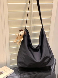 Detail of black nylon tote bag featuring a cute plush dog charm by a white shutter