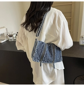 Crossbody denim shoulder bag with multiple functional zippers shown on a model back