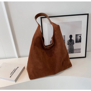 Detail of a brown suede hobo tote bag with a wide shoulder strap in a minimalist setting