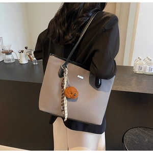 Gray canvas tote bag with black leather handles and bear charm worn by a model