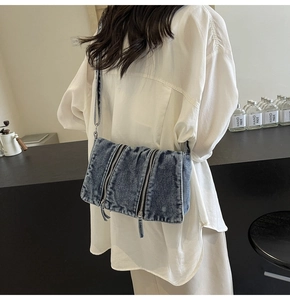 Detail view of washed blue denim crossbody bag with decorative triple vertical zippers