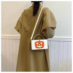 Detail view of small white square crossbody bag with orange pumpkin face on a model