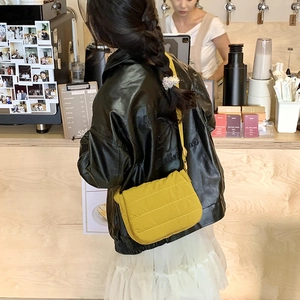 Ginger yellow quilted crossbody bag with adjustable strap worn by model in a cozy cafe setting