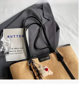 Close-up of brown suede tote bag featuring black leather trim and soft plush charm