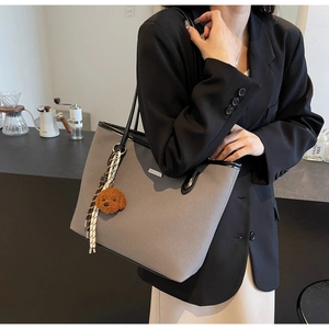 Detail view of a textured grey tote bag with black leather handles and a bear charm