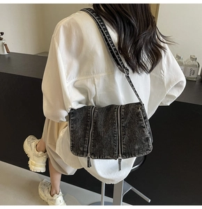 Detail view of retro black washed denim crossbody bag with silver zippers on a model