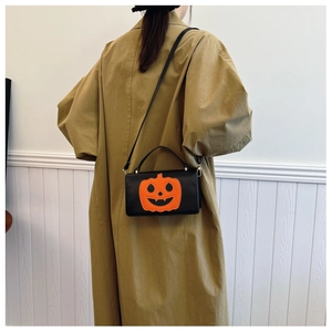 Close-up of black PU leather handbag with orange pumpkin pattern on khaki trench coat