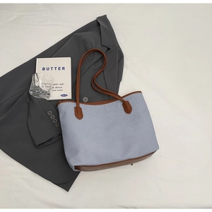 Minimalist light blue canvas tote bag with brown leather trim on grey suit background