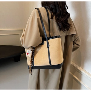 Detail of trendy patchwork tote bag in yellow corduroy and black leather with bear charm