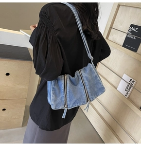Detail view of stylish blue denim shoulder bag with vertical zippers and long straps