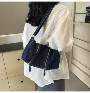 Detail view of washed blue denim shoulder bag featuring dual silver zipper hardware
