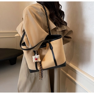 Detail of khaki tote bag with black trim, fashion label, and cute plush lamb charm