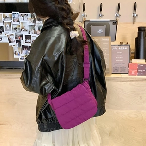 Detail view of purple quilted crossbody bag with wide shoulder strap in a cafe setting