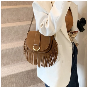 Close-up of brown fringe saddle bag with golden U-buckle worn with a white blazer