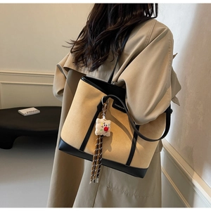 Close-up of camel suede tote bag with black leather trim and white plush charm detail