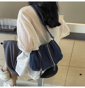 Detail of a dark blue denim shoulder bag with vertical zippers shown on a model