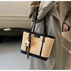 Detail view of stylish beige PU leather tote bag with black trim and plush bear charm