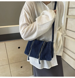 Detail view of a dark blue denim crossbody bag featuring metal zippers and workwear style
