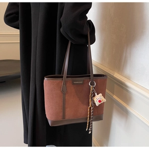Brown suede tote bag with leather strap and metal logo tag worn by a model in black