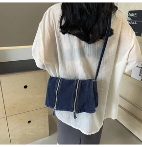 Deep blue denim crossbody bag with silver zippers shown on shoulder for size reference