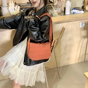 Quilted crossbody bag in orange-red nylon fabric worn by model at a coffee bar counter