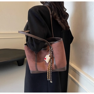 Detail view of brown suede tote bag with plush charm and side profile on shoulder