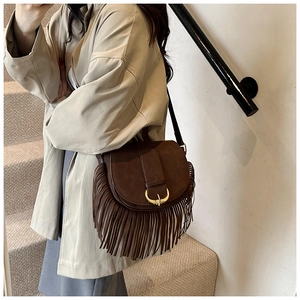 Detail showing the horseshoe buckle and long fringe on the dark brown suede saddle bag