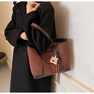 Detail view of suede tote bag with leather trim and toast plush charm accessory