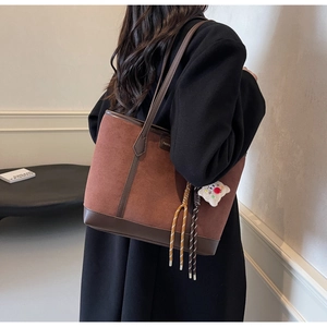 Detail of reddish-brown suede tote bag with brown leather trim and plush charm