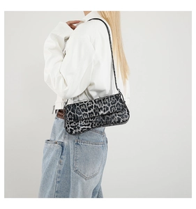 Close-up of leopard print baguette bag with long strap worn by a model in studio